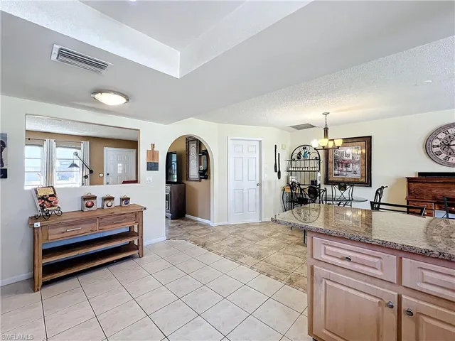 Kitchen with a textured ceiling, light tile patterned floors, hanging light fixtures, dark stone countertops, and a chandelier