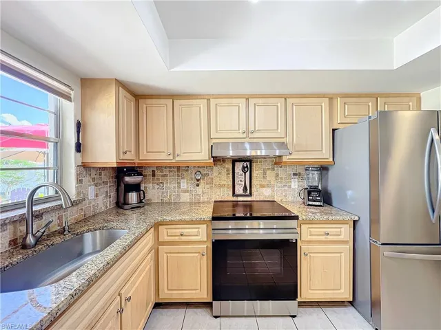 Kitchen with tasteful backsplash, appliances with stainless steel finishes, light tile patterned floors, light brown cabinetry, and sink