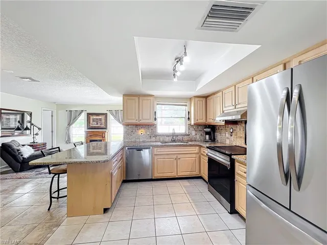 Kitchen featuring appliances with stainless steel finishes, a raised ceiling, sink, a kitchen breakfast bar, and kitchen peninsula