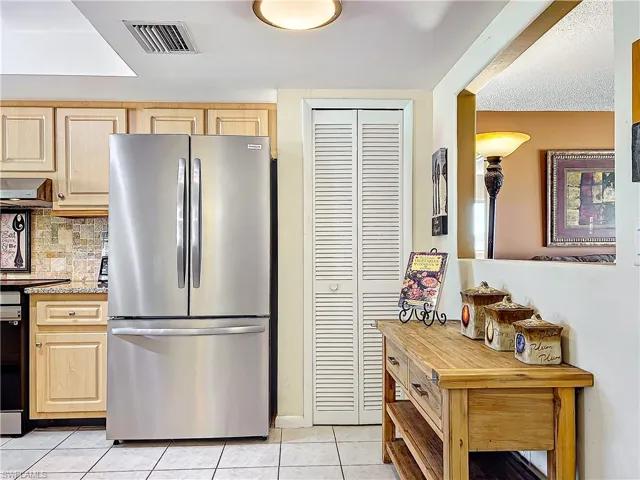 Kitchen featuring light brown cabinetry, exhaust hood, light tile patterned floors, and stainless steel fridge