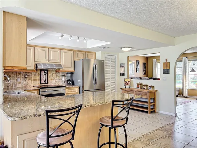 Kitchen featuring stainless steel appliances, sink, tasteful backsplash, light stone countertops, and light brown cabinetry