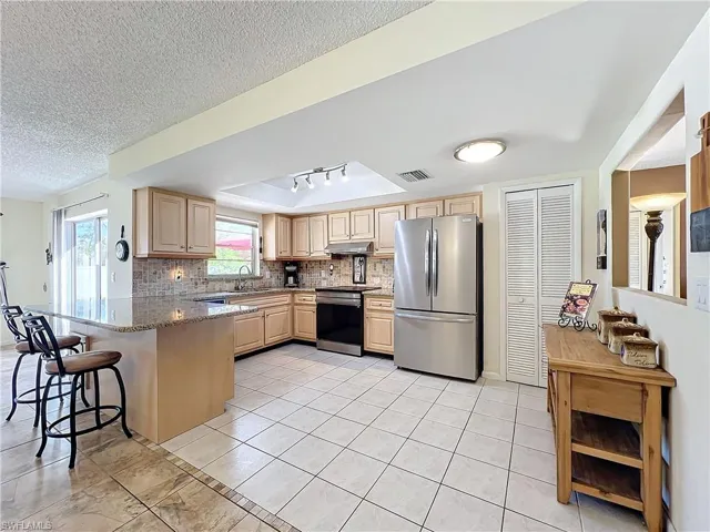 Kitchen with kitchen peninsula, light stone counters, appliances with stainless steel finishes, tasteful backsplash, and a kitchen bar