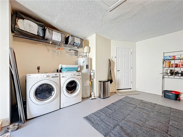 Laundry room featuring electric water heater, a textured ceiling, and washer and clothes dryer