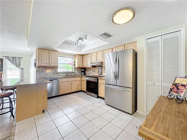 Kitchen with stainless steel appliances, backsplash, light brown cabinets, sink, and a breakfast bar