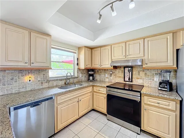 Kitchen featuring light tile patterned flooring, sink, appliances with stainless steel finishes, light brown cabinets, and decorative backsplash