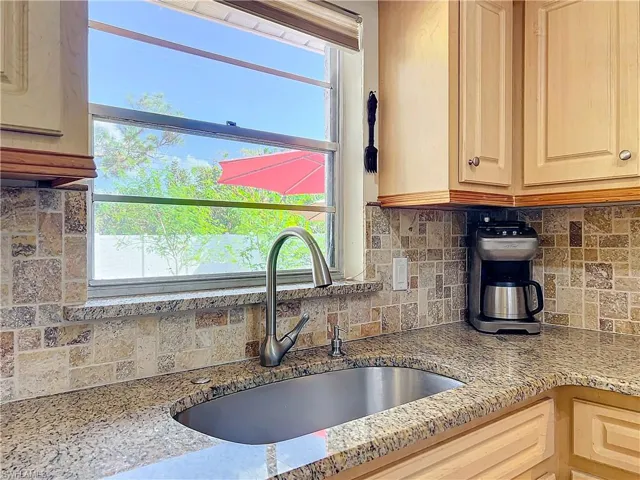 Kitchen with light brown cabinets, light stone countertops, sink, and tasteful backsplash
