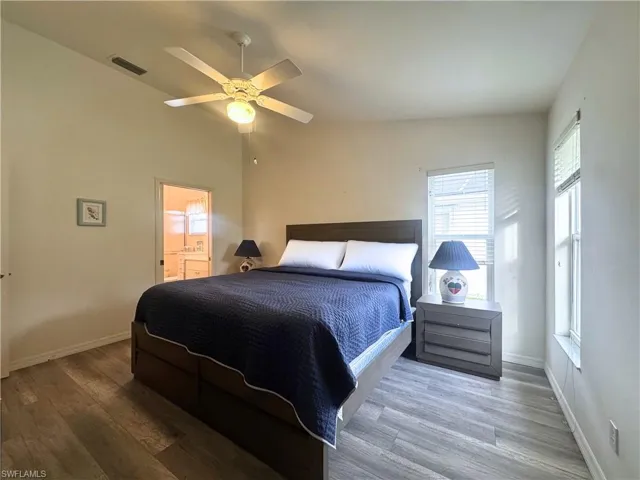 Bedroom with wood finished floors, ceiling fan, connected bathroom, and vaulted ceiling