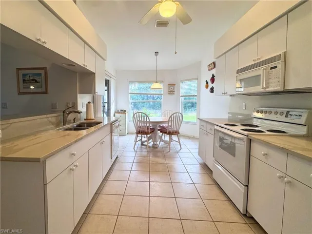 Kitchen featuring white appliances, light tile patterned floors, hanging light fixtures, ceiling fan, and white cabinetry