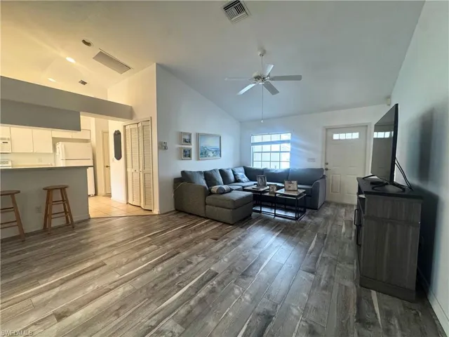 Living area with high vaulted ceiling, ceiling fan, and dark wood-style floors