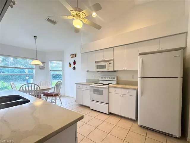 Kitchen featuring white appliances, lofted ceiling, white cabinets, hanging light fixtures, and a ceiling fan