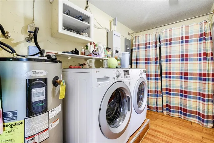 Laundry area with washer and dryer, electric water heater, a textured ceiling, and light hardwood / wood-style flooring! Lots of storage