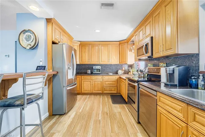 Kitchen with dark stone counters, light hardwood / wood-style flooring, light brown cabinetry, tasteful backsplash, and appliances with stainless steel finishes