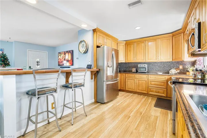 Kitchen featuring backsplash, a breakfast bar, light hardwood / wood-style floors, and appliances with stainless steel finishes