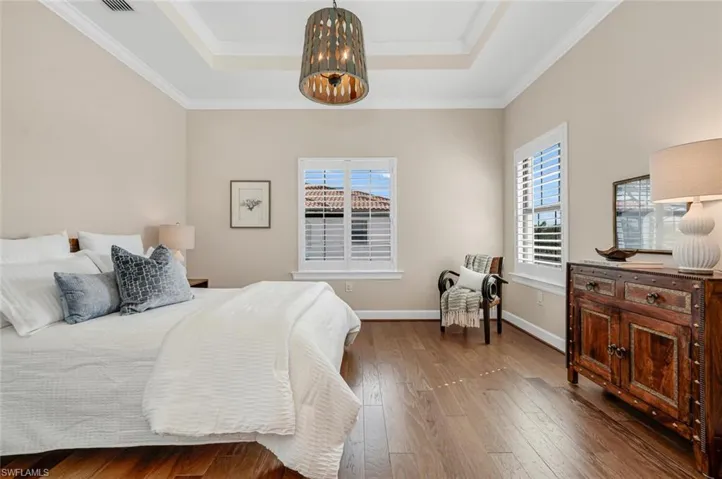 Bedroom with a raised ceiling, crown molding, hardwood / wood-style flooring, and a notable chandelier