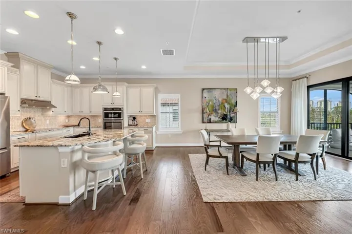 Kitchen with a breakfast bar, sink, hanging light fixtures, light stone countertops, and a center island with sink