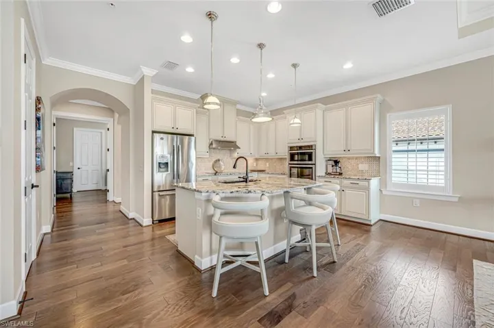 Kitchen with sink, light stone counters, decorative light fixtures, stainless steel appliances, and a kitchen island with sink