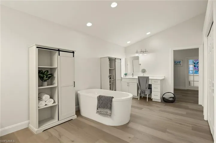 Bathroom featuring vanity, vaulted ceiling, wood-type flooring, and a tub to relax in