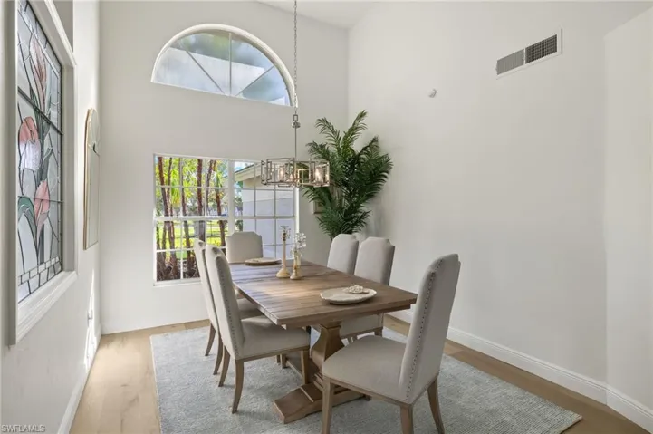 Dining space with light hardwood / wood-style flooring, a towering ceiling, a wealth of natural light, and an inviting chandelier