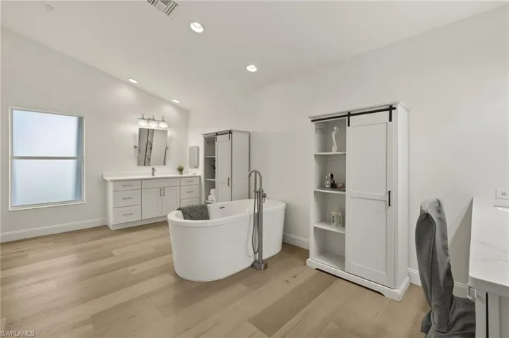Bathroom with vanity, lofted ceiling, a tub to relax in, and wood-type flooring