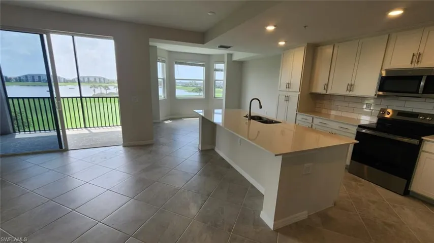 Modern kitchen featuring white cabinetry, a large center island with a sink, stainless steel appliances, and tile flooring