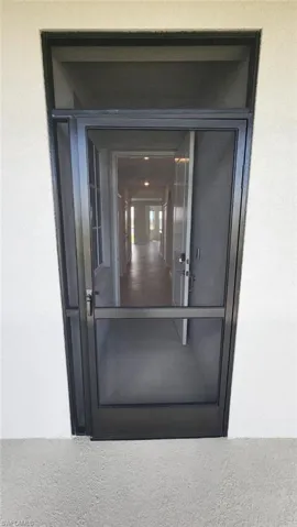 Entryway featuring a dark-framed screen door with a transom window, set against a light-colored stucco exterior
