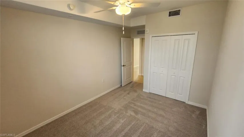 Carpeted interior room featuring neutral wall tones, a ceiling fan with integrated lighting, and a bi-fold closet
