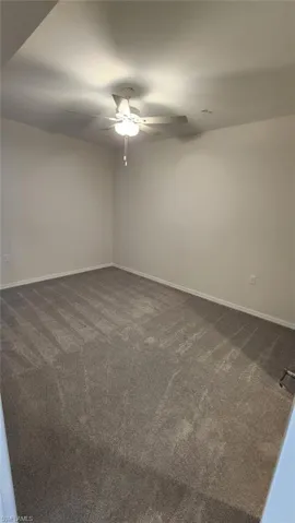Spacious room featuring gray carpet, light neutral wall paint, and a ceiling fan with integrated lighting
