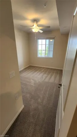 Carpeted room featuring a ceiling fan with integrated lighting, a window with vertical mullions, and neutral wall tones