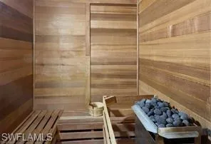 Dedicated sauna room featuring slatted wood benches, natural wood plank walls, and a stone-filled heating element
