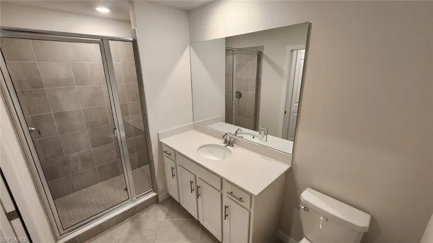 Bathroom featuring a glass-enclosed shower with large format tile, a vanity with a single sink and under-cabinet storage, and a frameless wall mirror