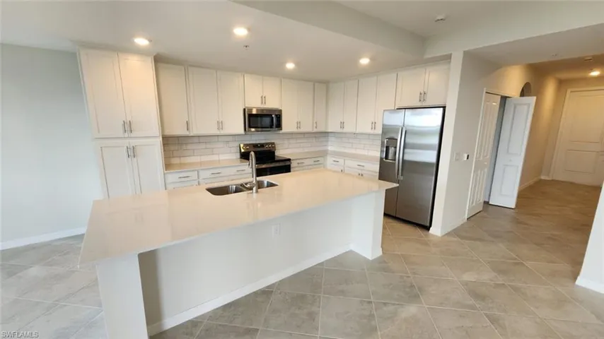Contemporary kitchen featuring white cabinetry, a large island with a dual-basin sink, stainless steel appliances, a subway tile backsplash, and recessed lighting