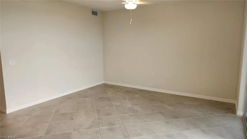 Expansive room featuring large format neutral-toned floor tiling, light beige wall paint, white baseboards, and a ceiling fan with integrated lighting