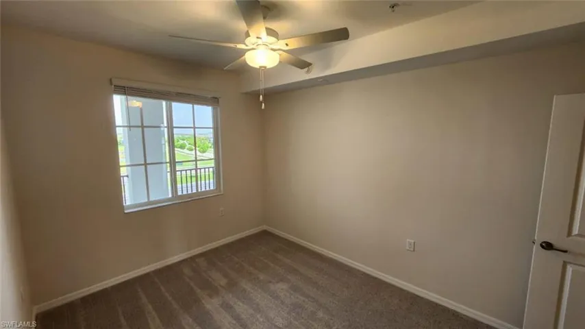 Neutral-toned room featuring a window with integrated blinds, a ceiling fan with light, and textured carpeting