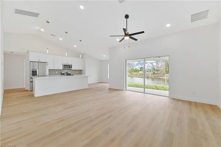 Unfurnished living room with recessed lighting, light wood-style flooring, a ceiling fan, lofted ceiling, and a water view