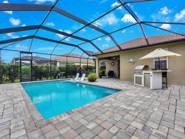View of swimming pool featuring glass enclosure, ceiling fan, a grill, a patio area, and exterior kitchen