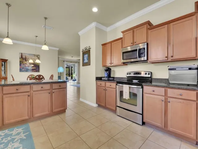 Kitchen with crown molding, light tile patterned floors, decorative light fixtures, and appliances with stainless steel finishes