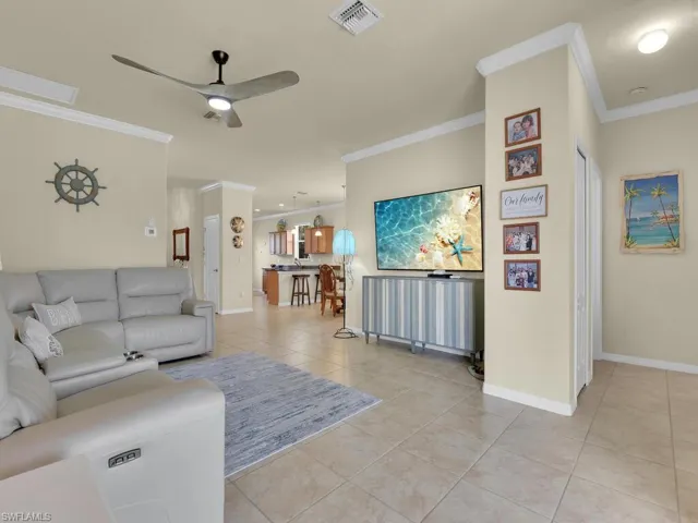 Living room with ceiling fan, ornamental molding, and light tile patterned flooring
