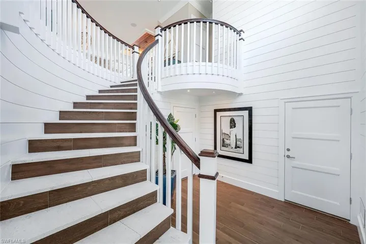 Stairway with wood finished floors, a towering ceiling, wood walls, and baseboards