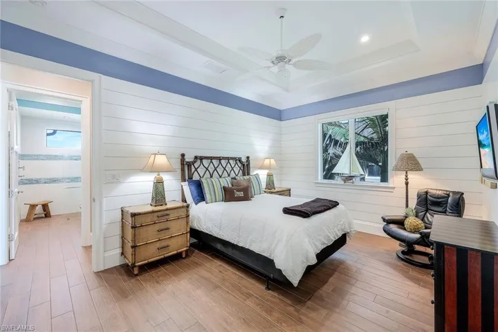 Bedroom featuring a raised ceiling, multiple windows, wood finished floors, a ceiling fan, and wood walls
