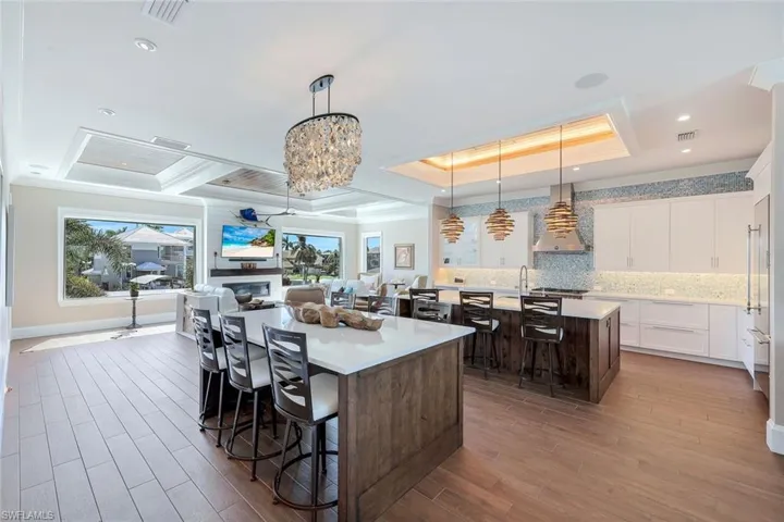 Kitchen featuring a kitchen island with sink, a tray ceiling, wall chimney range hood, a breakfast bar area, and light countertops