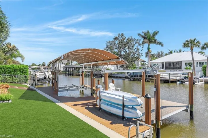Dock with boat lift, a water view, and a lawn