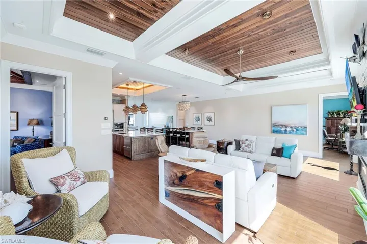 Living room with a raised ceiling, wooden ceiling, light wood-style flooring, a ceiling fan, and a chandelier