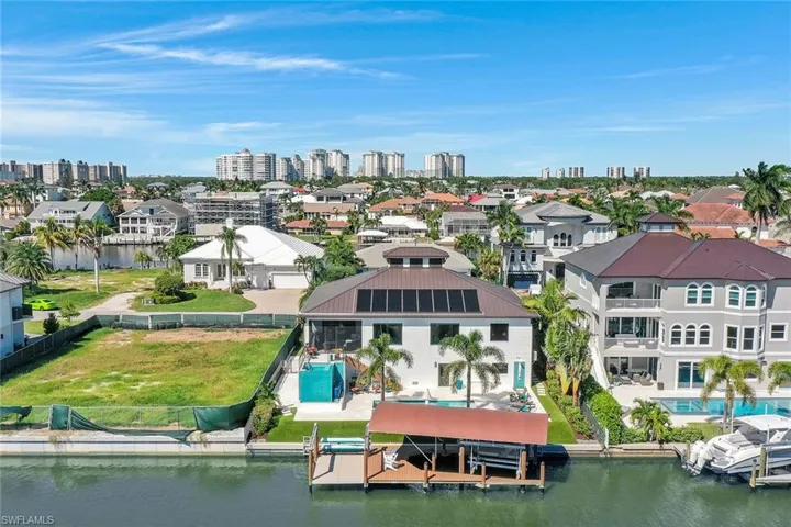 Aerial perspective of suburban area featuring a pool, a nearby body of water, and a skyline view