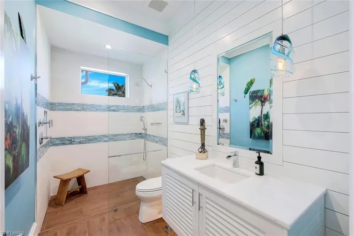 Bathroom featuring a tile shower, toilet, wood finished floors, vanity, and tile walls