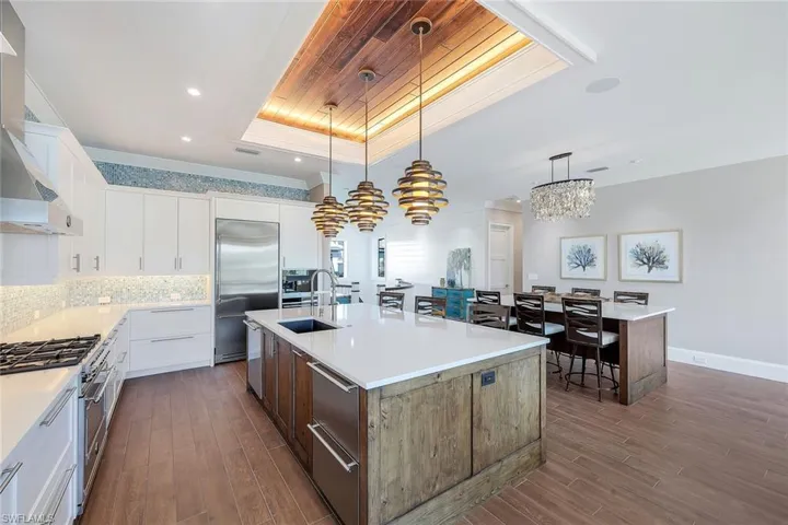 Kitchen with high end appliances, a tray ceiling, a kitchen island with sink, wall chimney range hood, and a sink