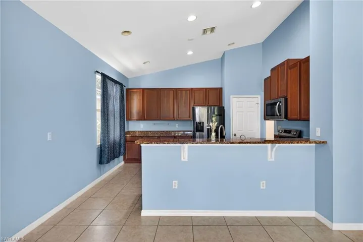 Kitchen featuring a kitchen breakfast bar, stainless steel appliances, dark stone counters, a peninsula, and wood finish cabinets