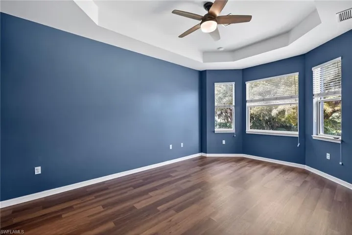 Spare room with a raised ceiling, ceiling fan, and dark wood-style flooring