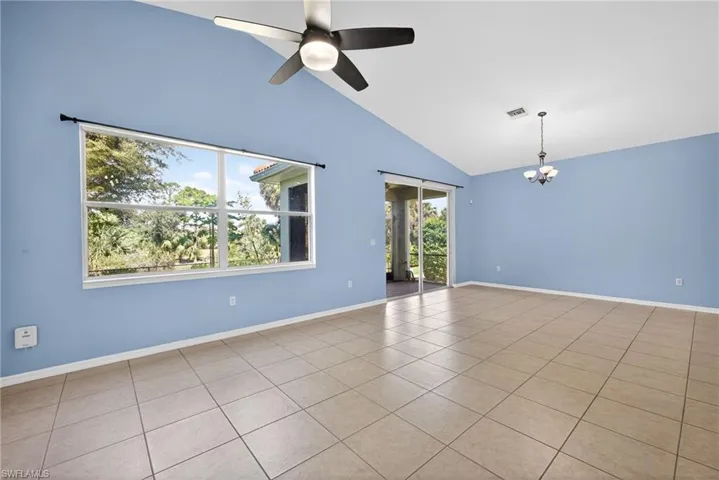 Empty room featuring hanging lights, vaulted ceiling, tile patterned floors, and a ceiling fan