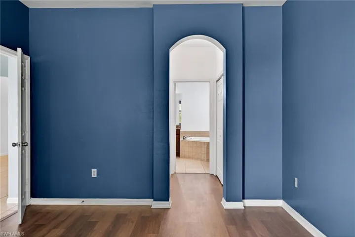 Unfurnished bedroom with arched walkways, dark wood-type flooring, and connected bathroom