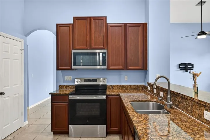 Kitchen with stainless steel appliances, dark stone counters, light tile patterned floors, a ceiling fan, and arched walkways